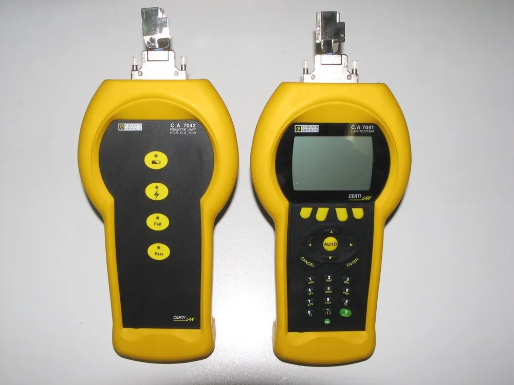 Two yellow handheld instruments lying on a grey surface, each with a shielded socket for a network lead on the top edge. The unit on the right is labelled C.A 7041 LAN TESTER and has a large LCD screen, a row of soft keys beneath it, a circular navigation pad marked AUTO, CANCEL and ENTER, and a numeric keypad. The unit on the left is labelled C.A 7042 REMOTE UNIT FOR C.A 7041 and has no screen at all, only four indicator lamps, the lower two reading Fail and Pass. Both carry the brand name CERTI LAN.