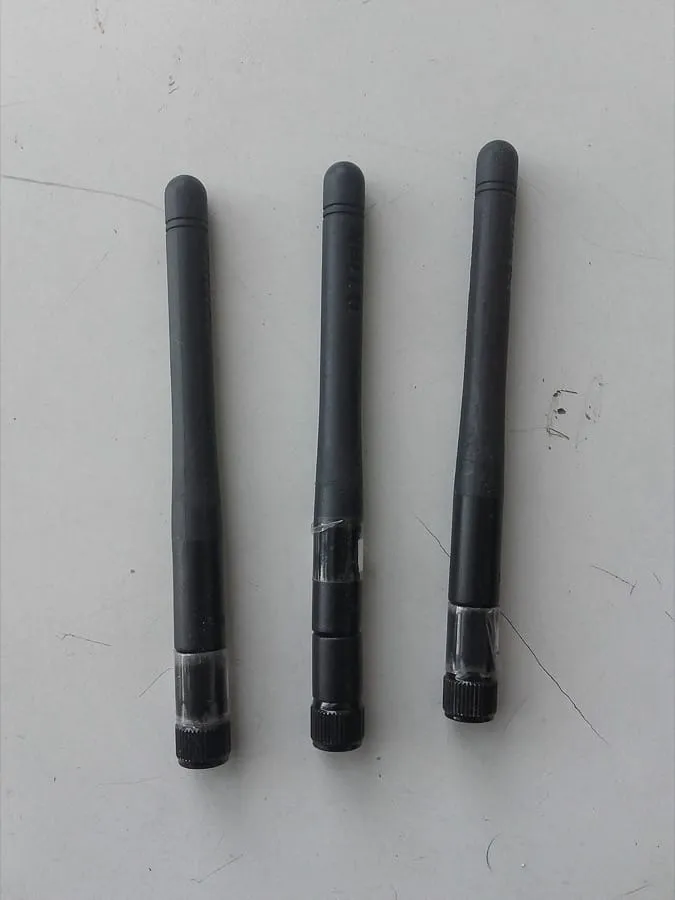 A pair of small black omnidirectional Wi-Fi antennas on a desk, each a slim rod about a hand’s length with a threaded connector at its base.