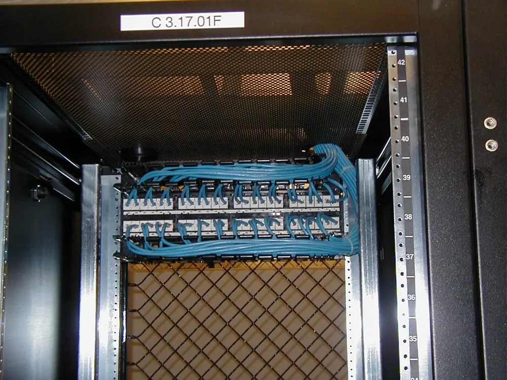 The rear of a patch panel inside an open rack. A bundle of identical blue cables arrives from above, fans out along a horizontal management bar, and each one is punched down onto a numbered block on the back of the panel. Every cable is dressed to the same curve and secured at the same points. The vertical rack rail to the right is stamped with unit numbers running from 34 at the bottom to 42 at the top.