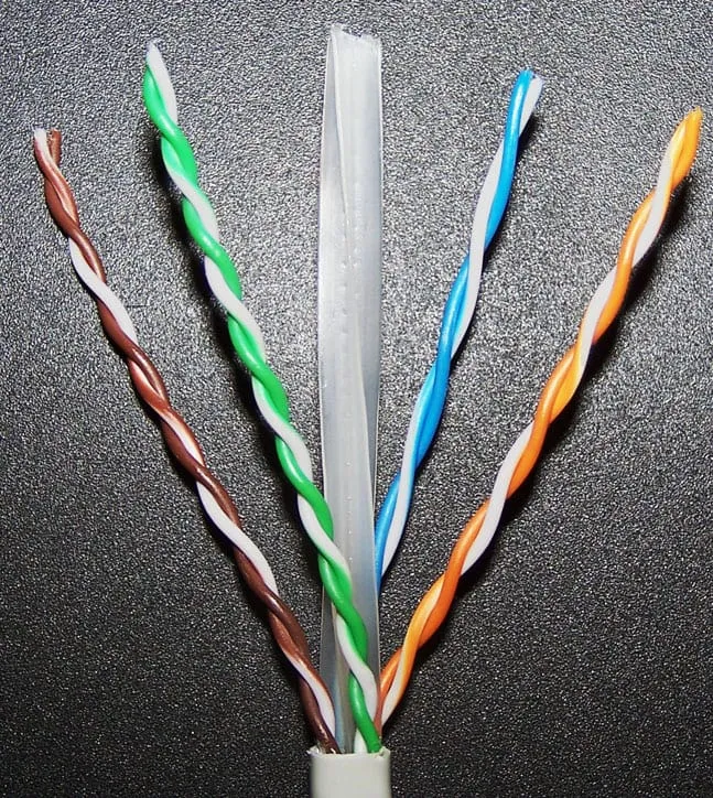 The jacket of a Category 6 cable cut back to expose four twisted pairs, coloured brown, green, blue and orange, each paired with a white wire of the same colour. The pairs are twisted at visibly different rates: the brown and orange pairs make roughly one turn per centimetre while the green pair turns noticeably more often over the same length. A grey plastic cross-shaped spine runs up the centre of the cable, holding the four pairs apart.